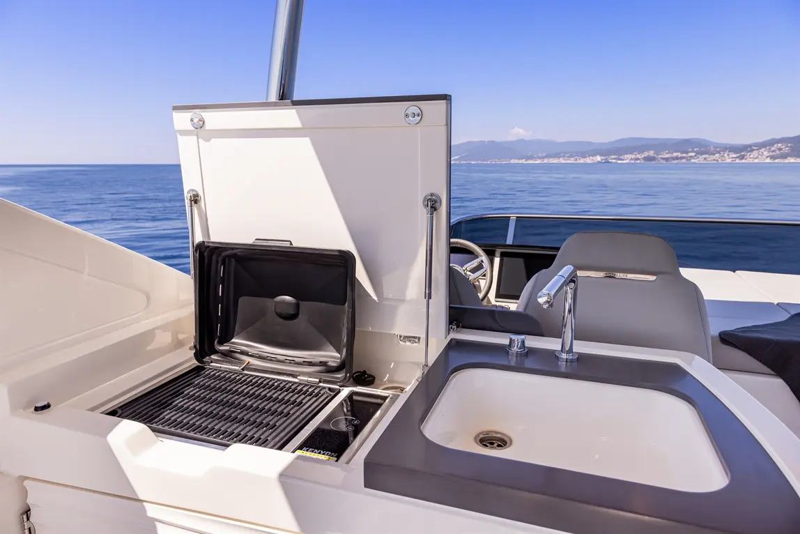 Sleek boat kitchen area featuring a grill, sink, and panoramic ocean views under a clear blue sky.